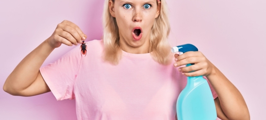 A woman is holding a cockroach trying to spray it