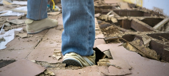 A person's foot has broken through a damaged wooden floor
